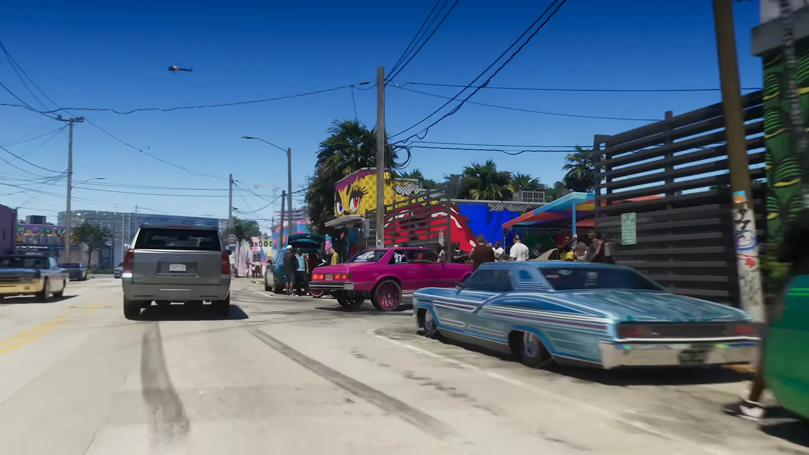 Stockyard in GTA VI: A Stockyard street car meet: lowriders and donks parked beside mural-covered warehouse walls.
